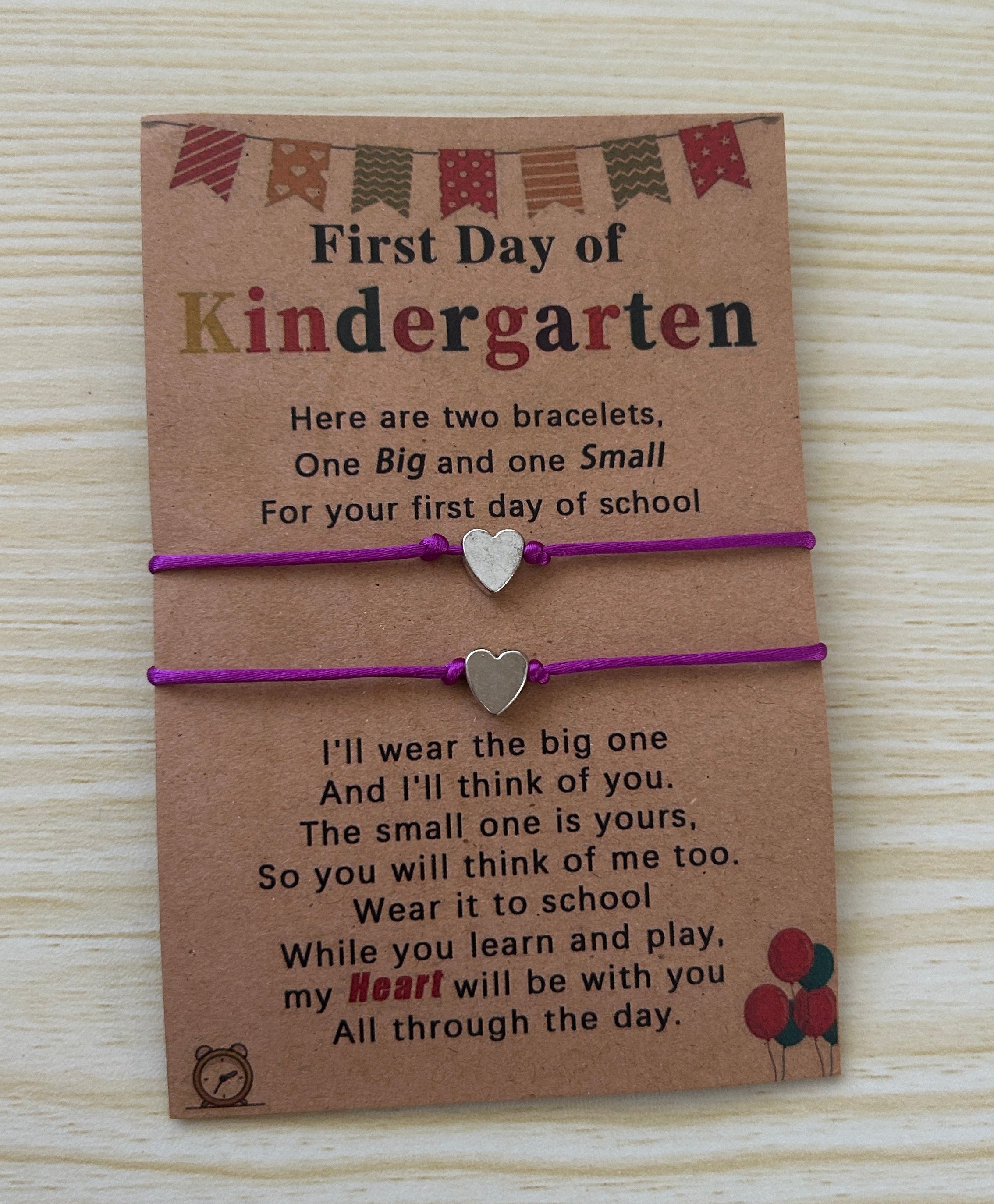 Two bracelets on a card with a message for the first day of kindergarten, displayed on a wooden surface.